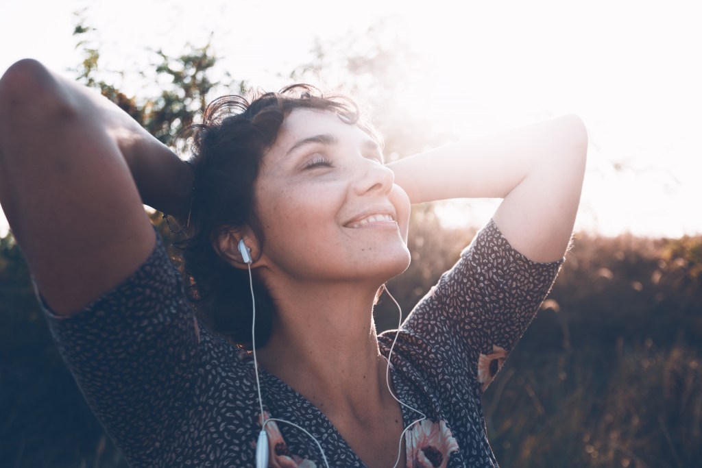 Smiling woman in headphones, resetting her dopamine and anxiety levels in the sun 