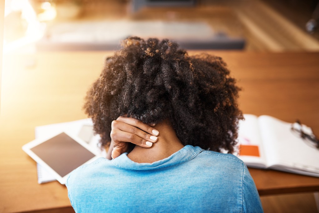 Emotional danger: back portrait of woman holding her neck while sitting at her office desk 