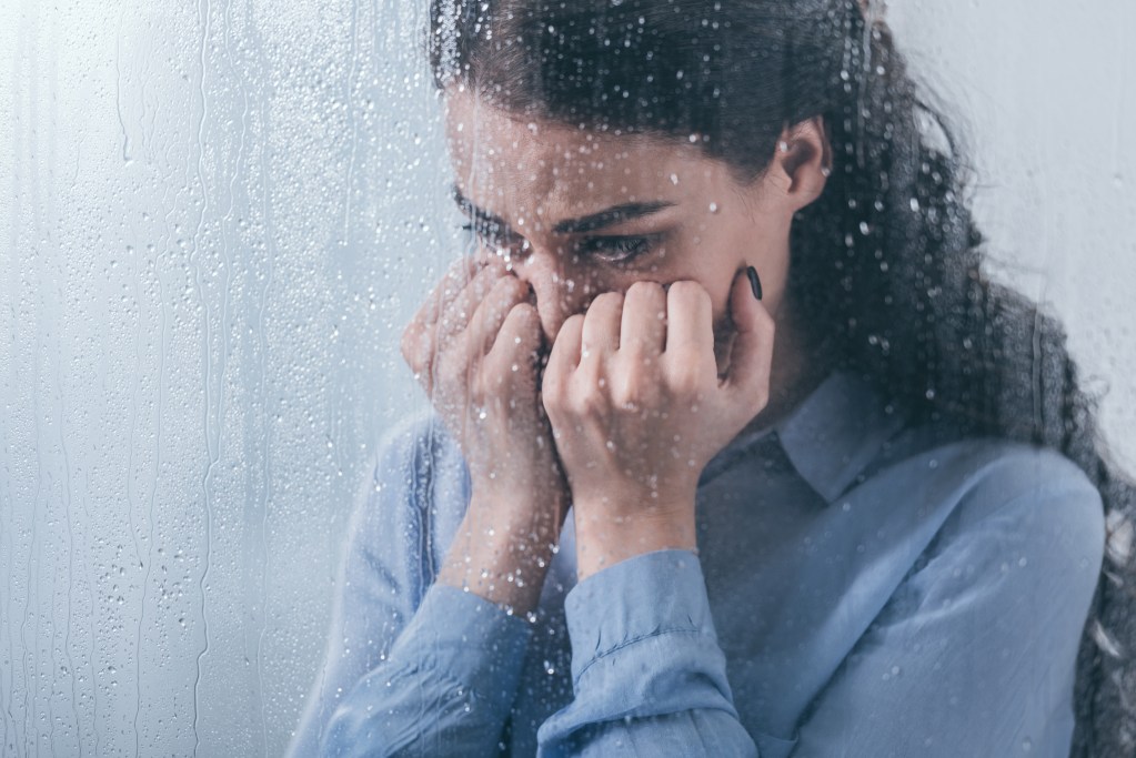 Woman at rainy window, struggling with winter blues, depression and anxiety
