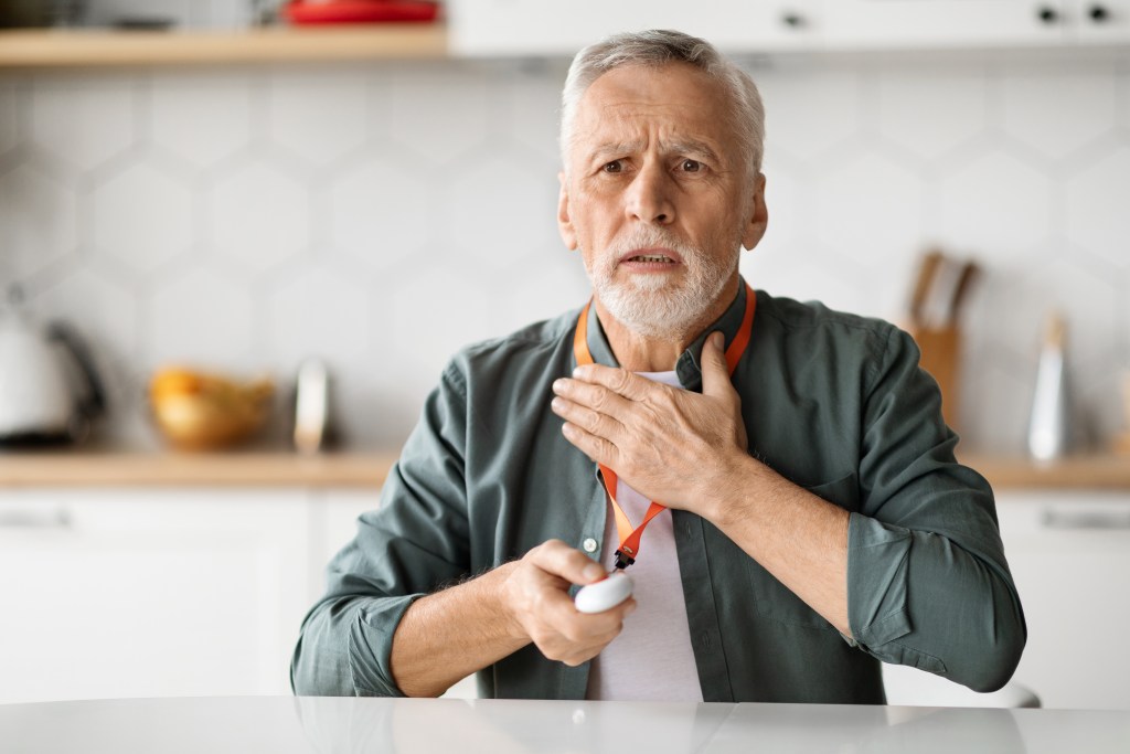 Senior touching his chest, pressing emergency button of medical alert system