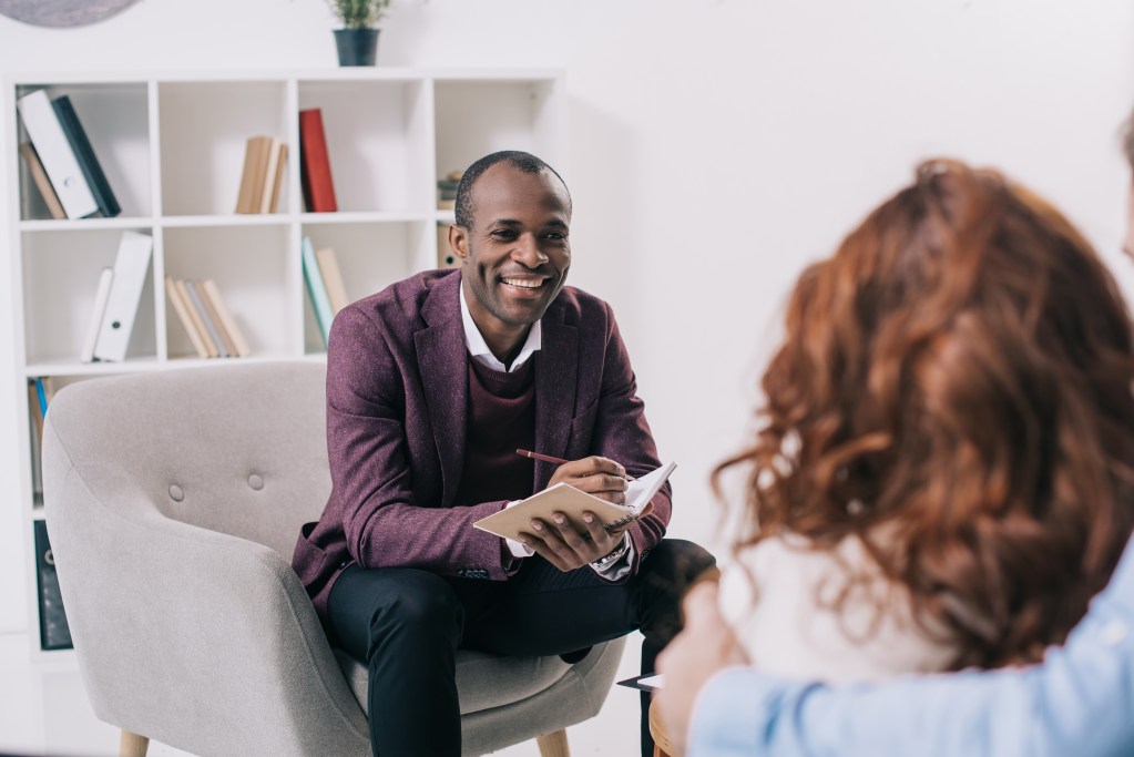 Smiling therapist taking notes from self-tracking patient in his office