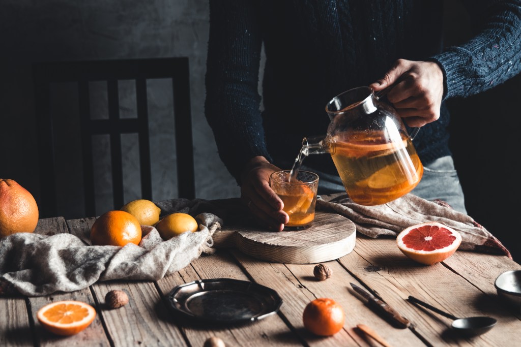 Functional beverages: A man pours mint-ginger-citrus tea on a wooden table. 