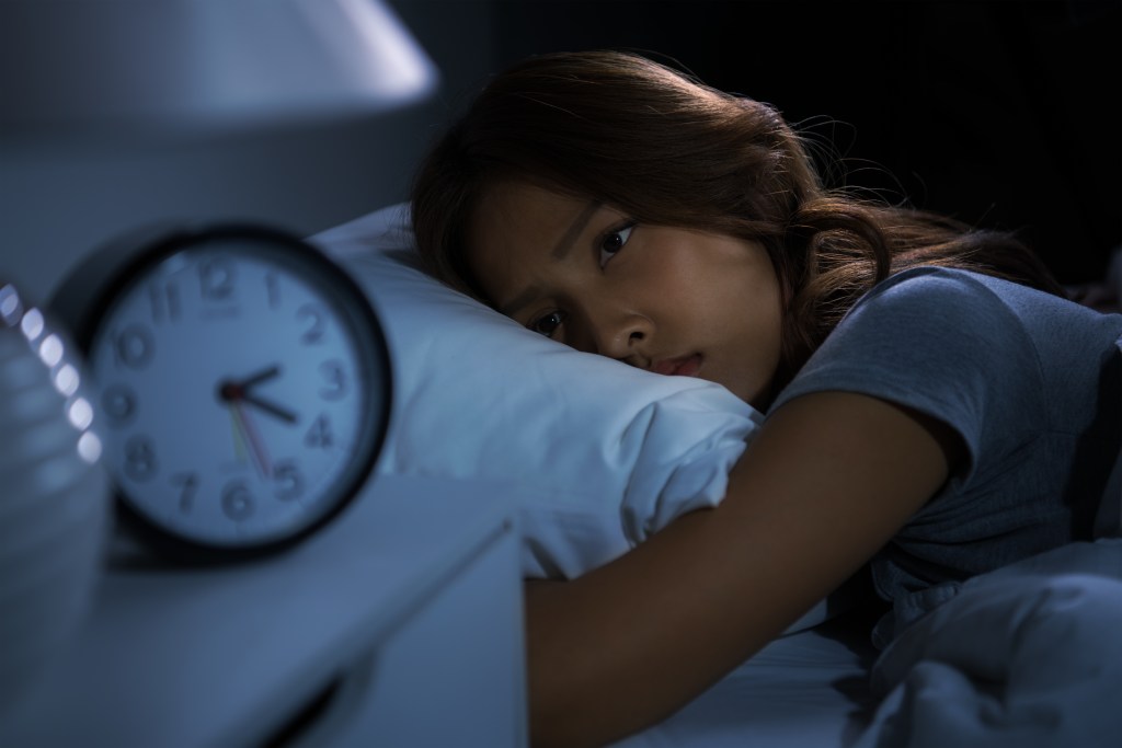 A woman in bed unable to fall asleep due to compounded chronic stress