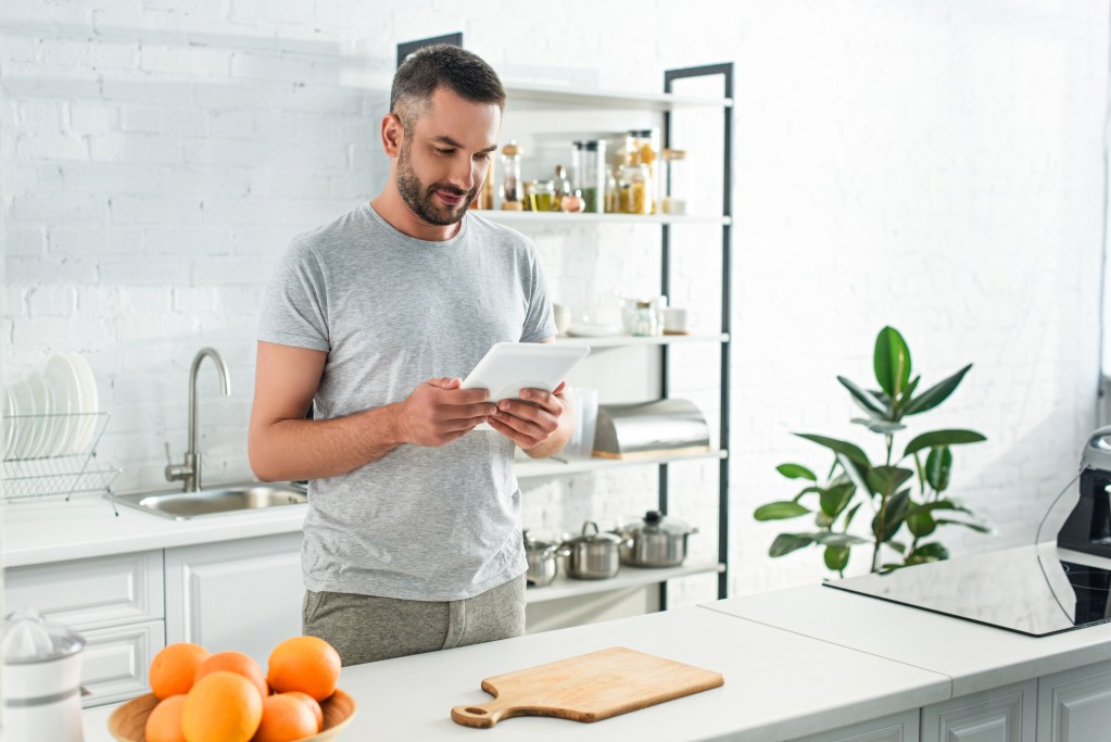 Man managing therapy sessions from his kitchen via digital tools. 