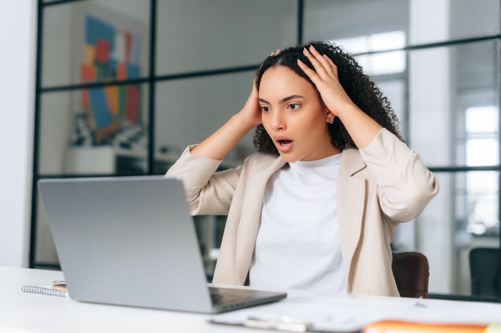 Shocked young woman, trying to recall file names, looking at chaos on laptop in office